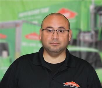 a man in a black shirt standing in front of a green SERVPRO truck