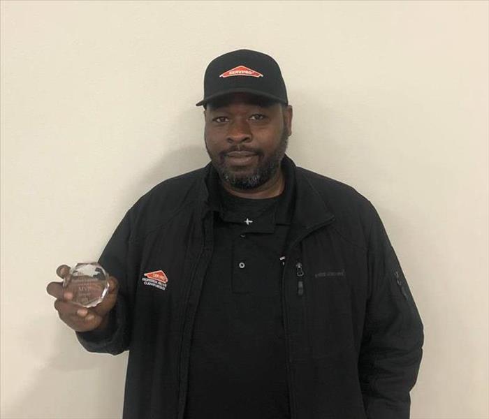 a man holding an award in front of a beige wall